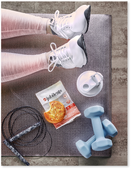 Woman on yoga mat with all her workout essentials including a Jubileats muffin 